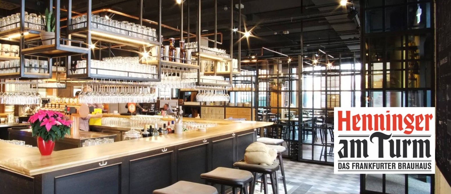 Moderne Bar mit industriellen Regalen voller Gläser und zwei Personen im Gespräch.