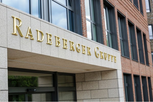 Goldene Buchstaben auf einem Gebäudeeingang über einem Glasportal zeigen einen Unternehmensnamen.