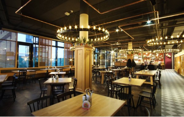 Ein modernes Restaurant mit Holztischen und dekorativer Beleuchtung ist beleuchtet.